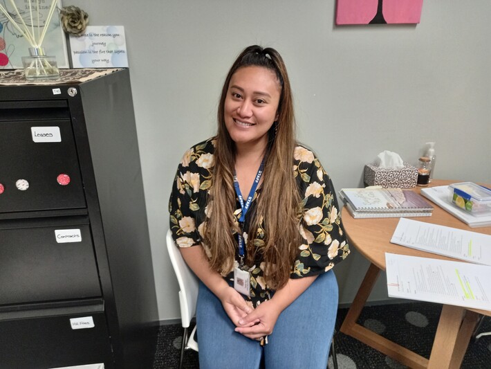 Tonia, a Somoan woman, sits in an Aviva office looking at the camera happily.