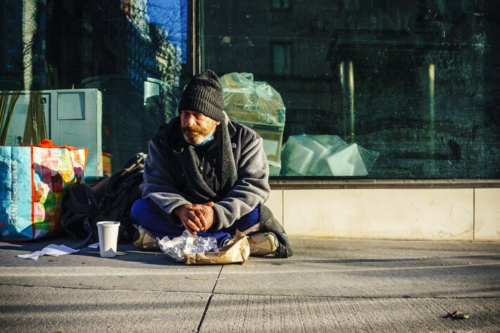 A homeless man bundled up for the cold outside a shop front